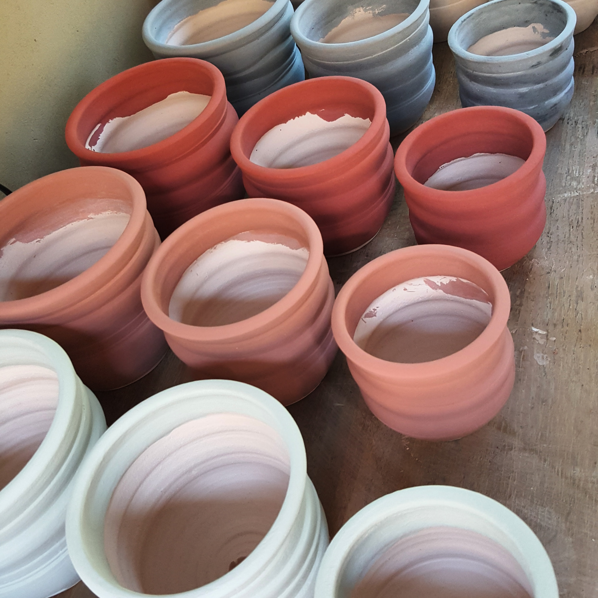 Grouped hand-thrown ceramic planters in terracotta, coral, and pale glaze, ready for firing